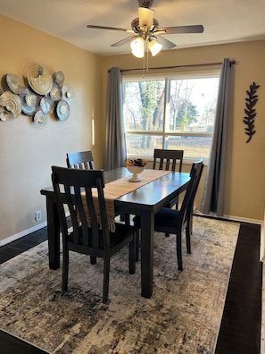 A dining area with a table, chairs, a ceiling fan, and a window with curtains.