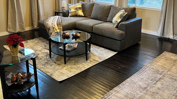 A living room with a sectional sofa, a glass coffee table, a rug, and large windows with curtains.