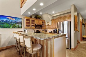 Eine Küche mit Holzschränken, einer Granit Arbeitsplatte, Edelstahlgeräten und einer Bar mit Sitzgelegenheiten.
