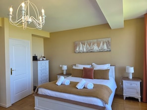 A bedroom with a bed, a chandelier, a dresser, a painting, and a nightstand.