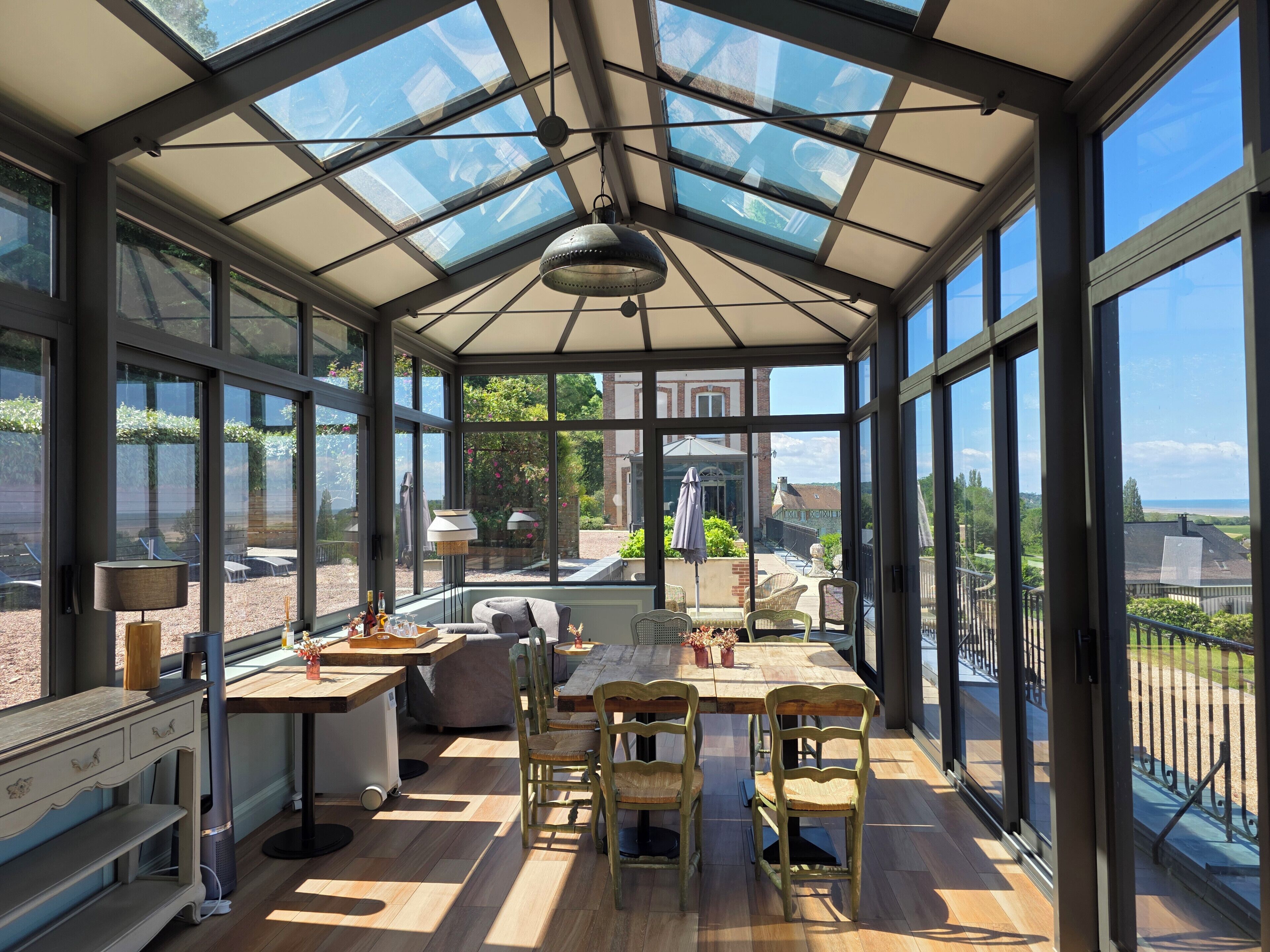 Een conservatorium met glazen dak, houten vloer en een eethoek met stoelen en tafel.