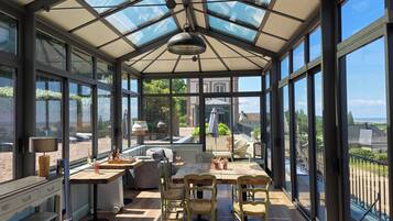 Een conservatorium met glazen dak, houten vloer en een eethoek met stoelen en tafel.