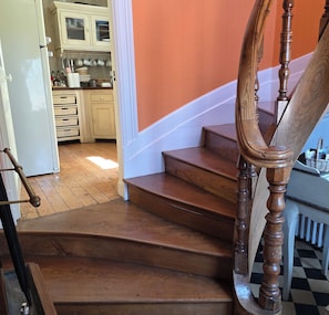 A wooden staircase with a handrail, leading to a kitchen area with cabinets and a countertop.
