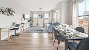 A modern living room with a dining area, large windows, and a view of the cityscape. - LuxBay Place 1BD/5 Min to Rutgers Newark/Pkg Incl (Newark)