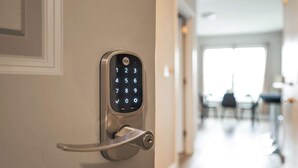 A Yale smart lock on a door with a keyhole, a hallway with a dining area in the background. - LuxBay Place 1BD/5 Min to Rutgers Newark/Pkg Incl (Newark)