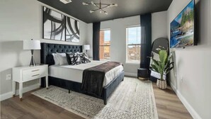 A modern bedroom with a large bed, a nightstand, a wall-mounted TV, and a large abstract painting. - LuxBay Place 1BD/5 Min to Rutgers Newark/Pkg Incl (Newark)