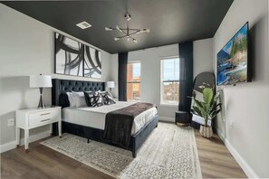 Ein modernes Schlafzimmer mit einem großen Bett, einem Nachttisch, einem an der Wand befestigten Fernseher und einem großen, abstrakten Gemälde.