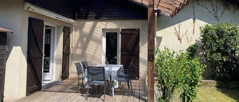 Une terrasse couverte avec une table et des chaises, un petit arbre et une plateforme en bois.