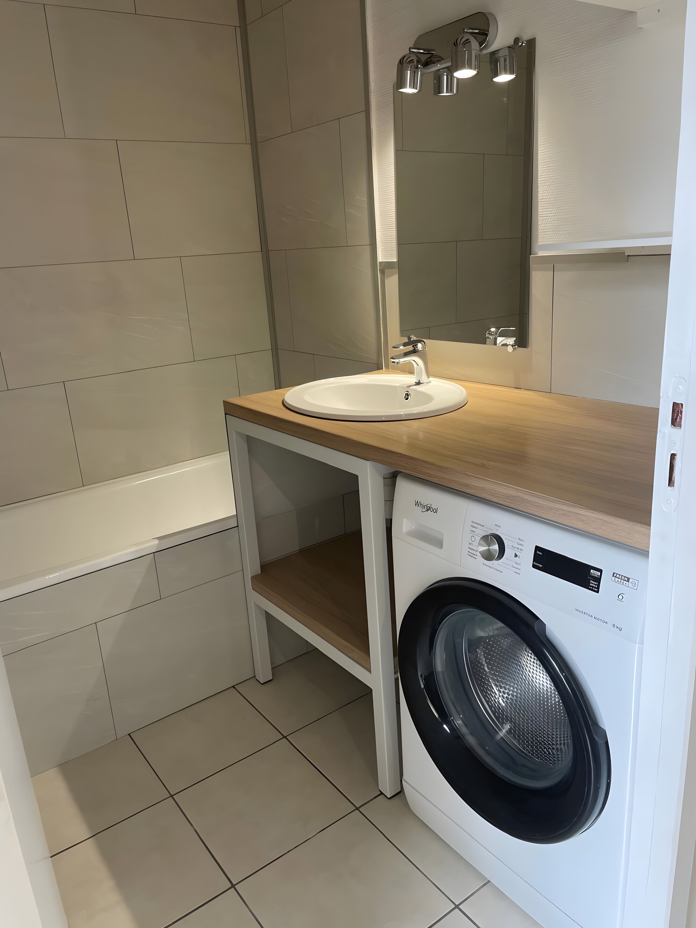 A compact bathroom with a sink, mirror, and a front-loading washing machine.