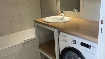 A compact bathroom with a sink, mirror, and a front-loading washing machine.