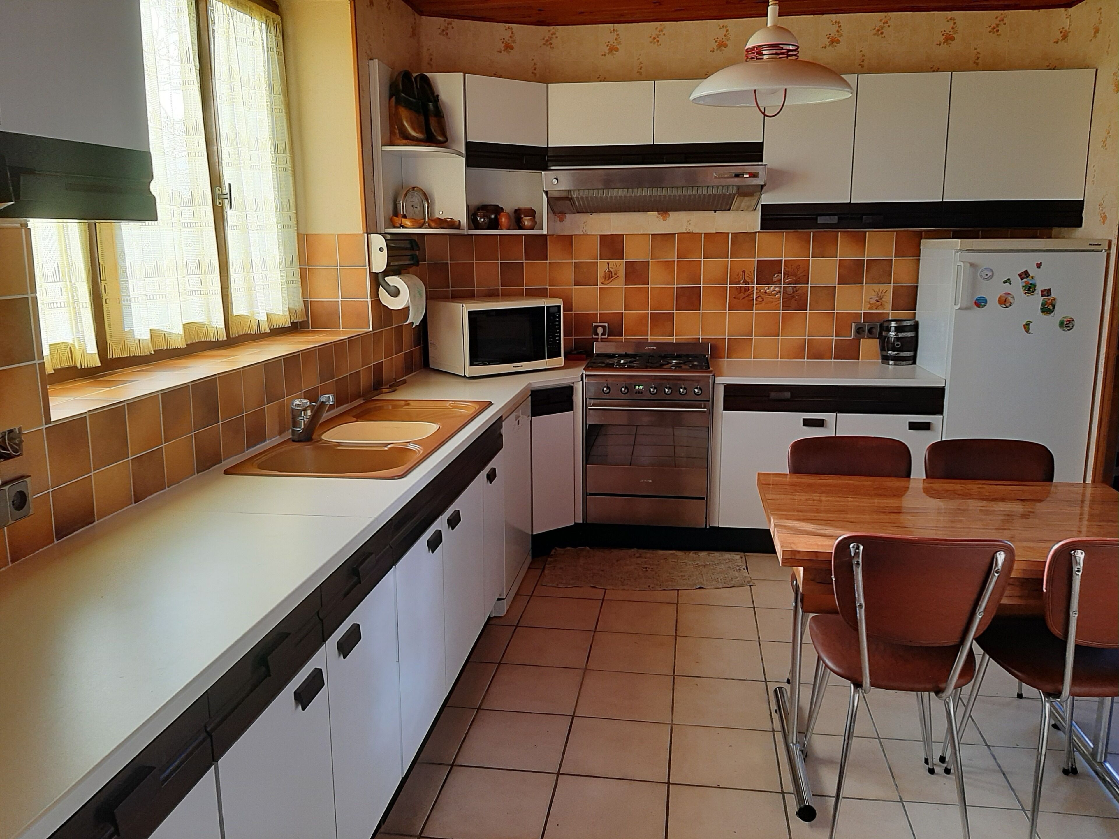 Een kleine keuken met een spoelbak, kookplaat, magnetron en een eethoek met stoelen.