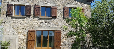 A stone building with wooden shutters, a large glass door, and a tiled roof.