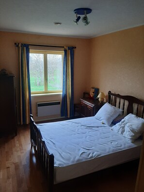 Ein Schlafzimmer mit einem Bett, einem Fenster mit Vorhängen, einem Heizkörper und einer Deckenleuchte.