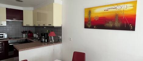 A modern kitchen with a dining area, a painting on the wall, and a table with a vase of flowers.