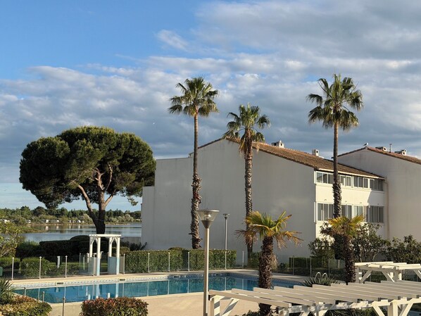 Ein Poolbereich mit einem Gebäude, Palmen und einem großen Baum.
