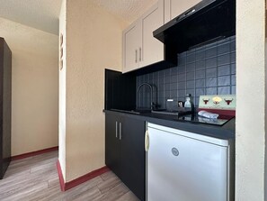 Eine kleine Küche mit schwarzem Arbeitsplatz, einem Edelstahlkühlschrank und einer gefliesten Spritzschutzwand.