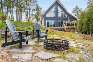 Eine Holzhütte mit einer Terrasse, zwei Adirondack-Stühlen und einer Feuerstelle.