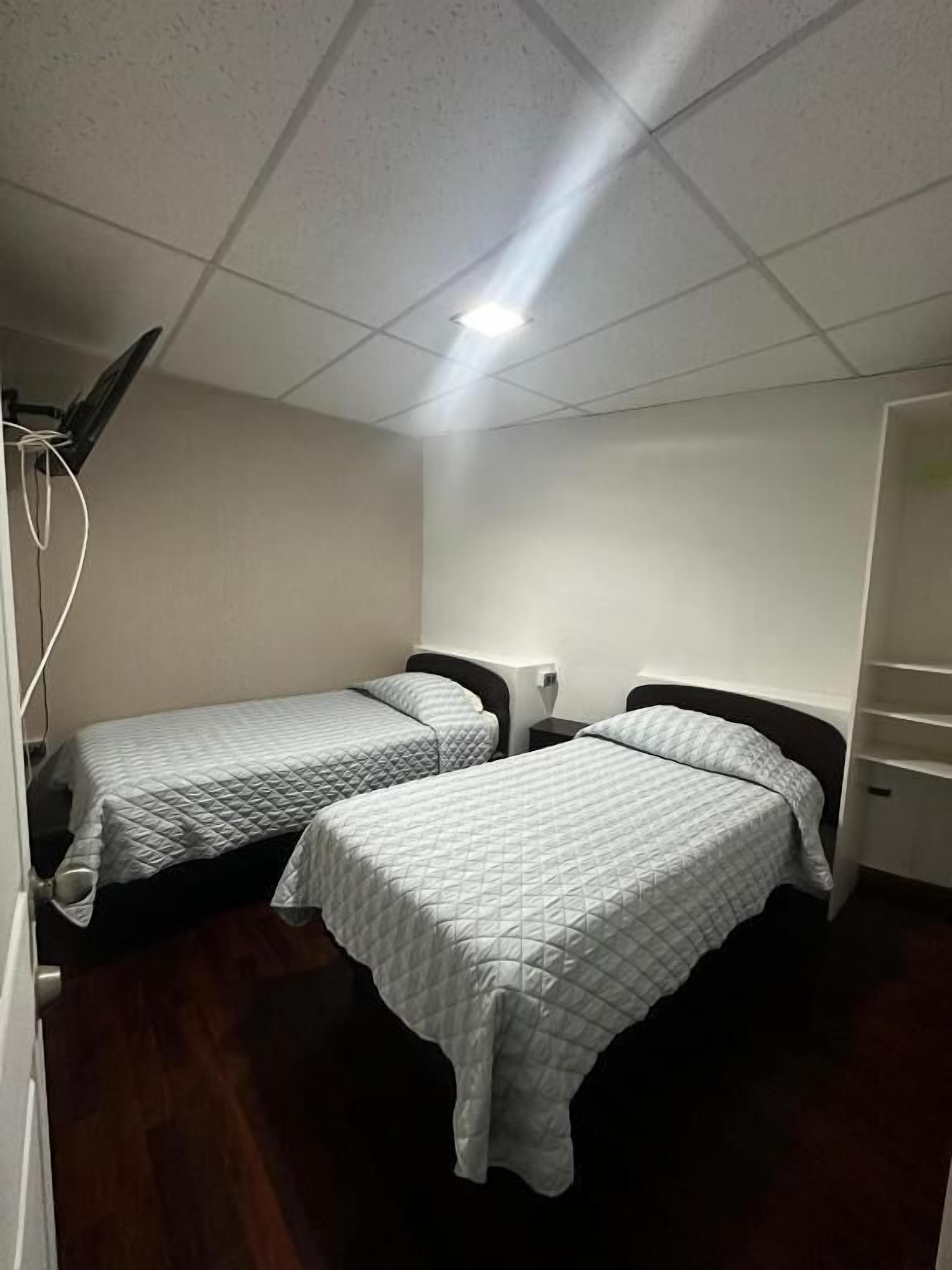 Una habitación de hotel pequeña y sencilla con dos camas individuales, un escritorio, una silla y un armario.