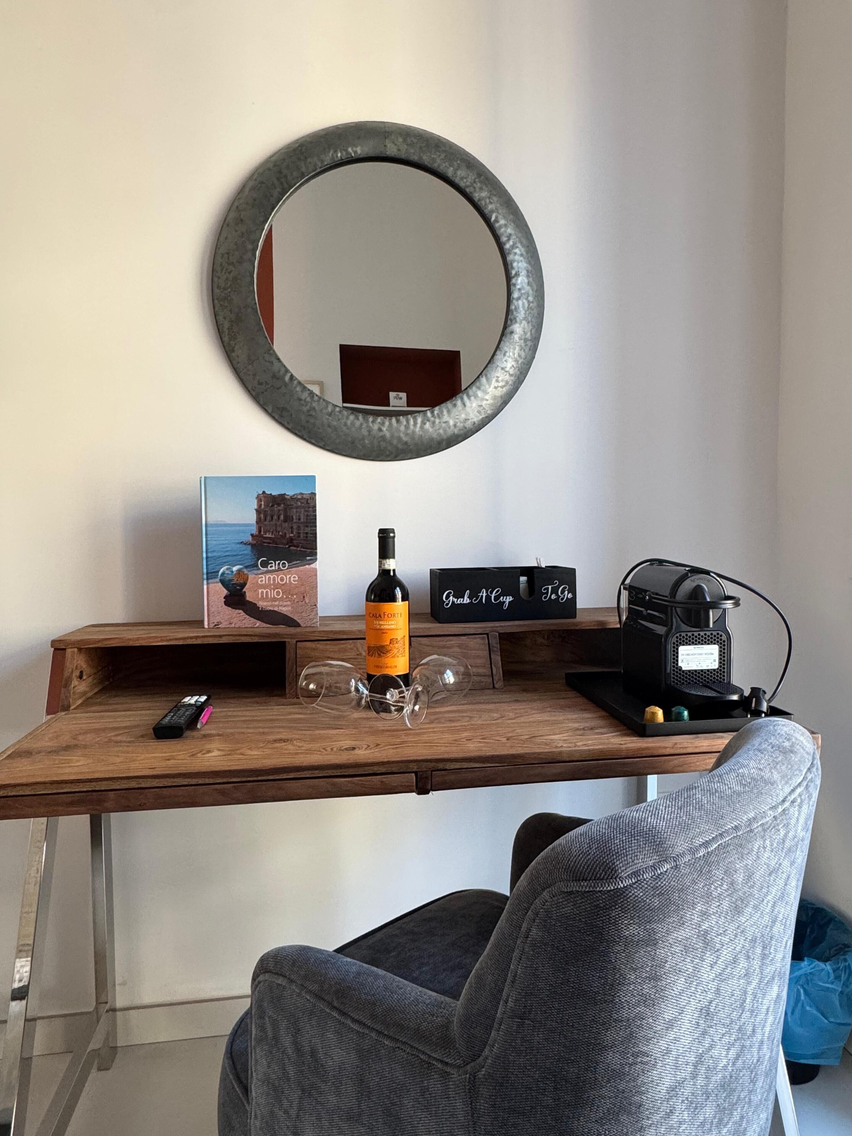 Un escritorio de madera con una botella de vino, dos copas, un control remoto, una cafetera y un cartel que dice 'Sirva una copa'.