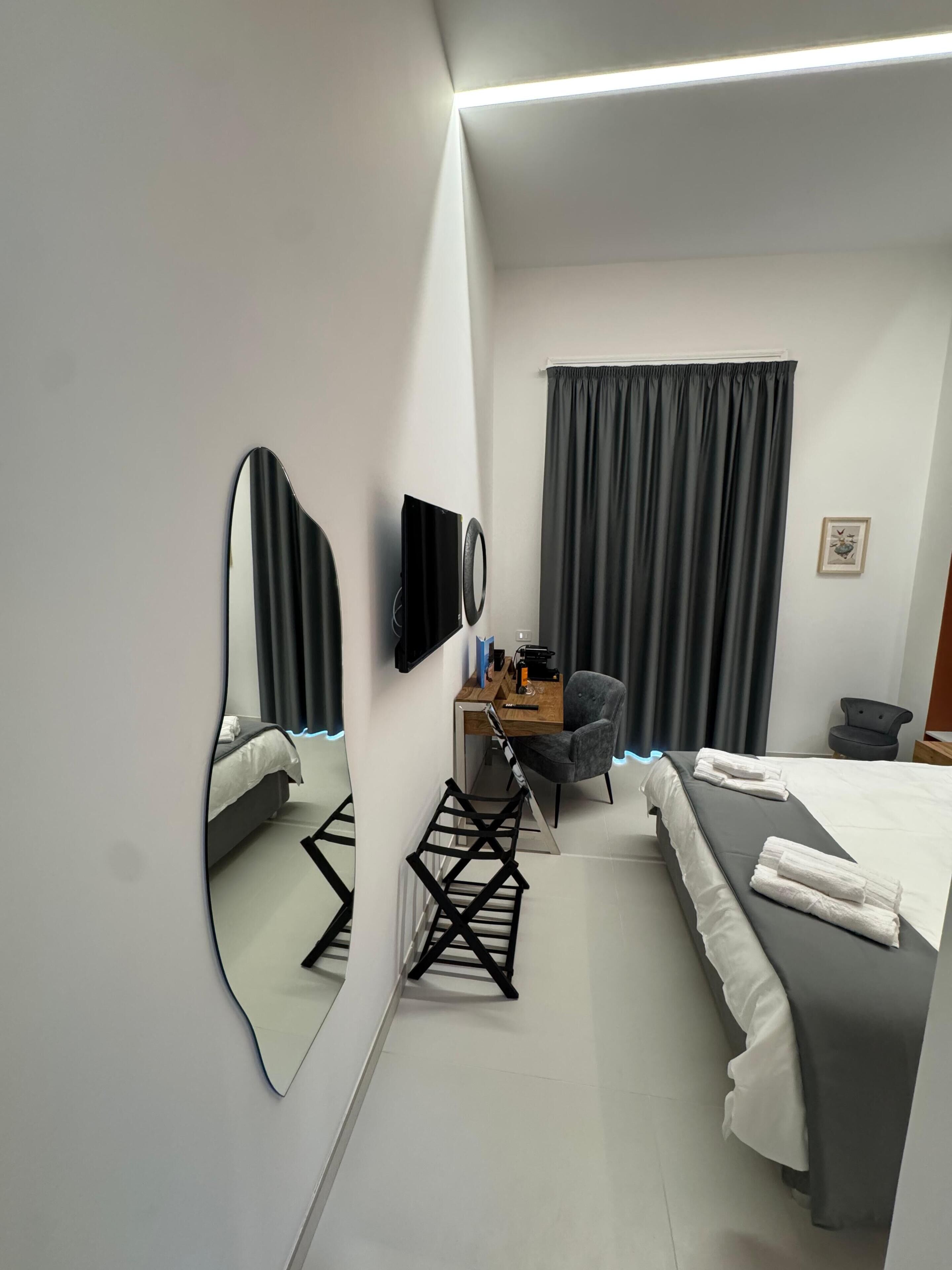 A modern hotel room with a bed, desk, chair, and a large mirror.