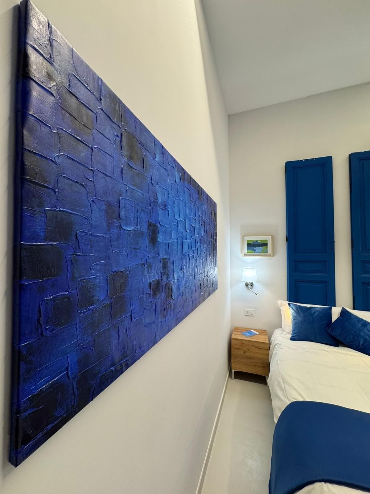 A room with a large blue textured wall, a bed with blue bedding, and two blue doors.