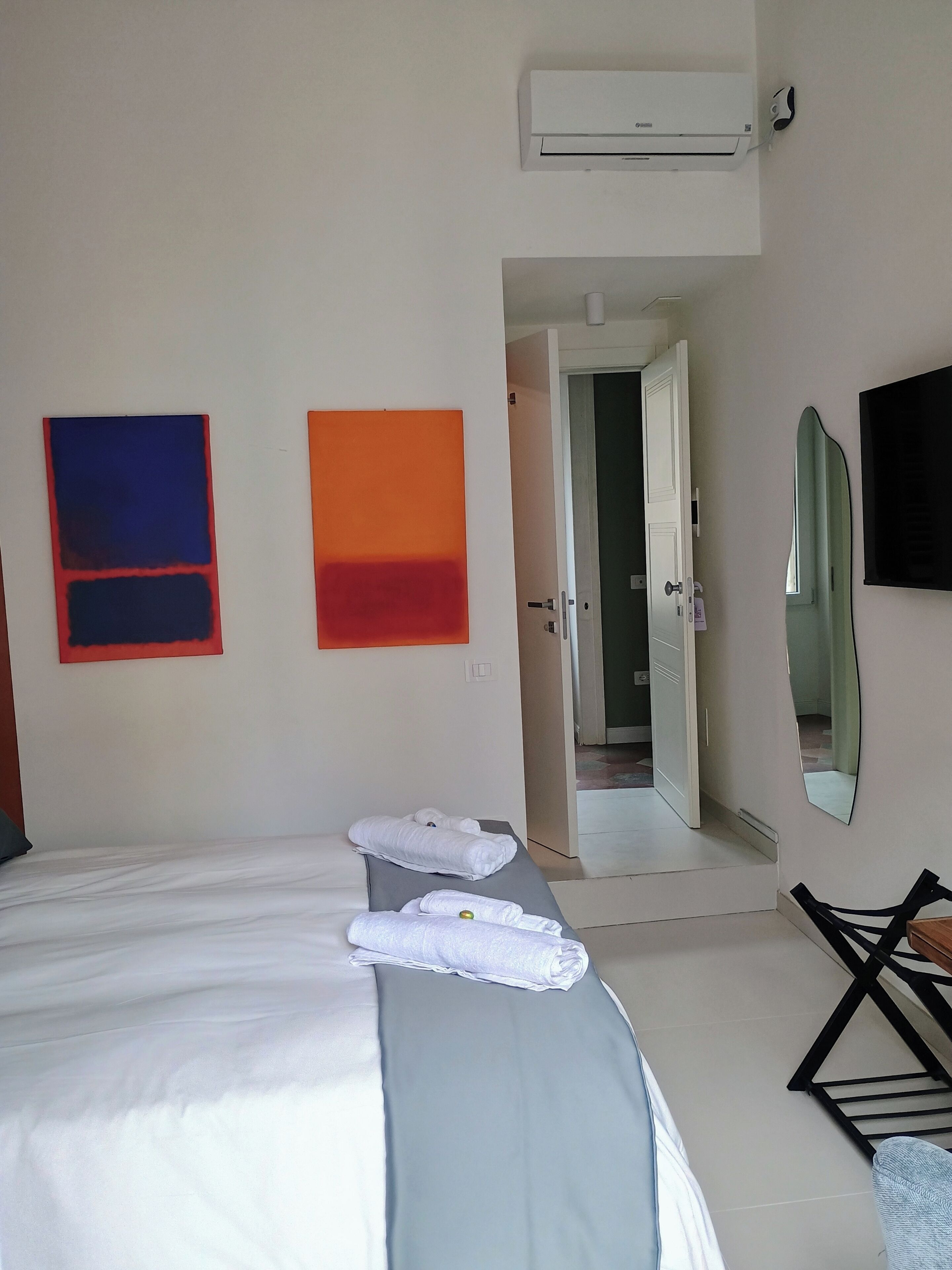 Une chambre d’hôtel équipée d’un lit, d’un bureau, d’une chaise, d’un climatiseur et de deux tableaux abstraits accrochés au mur.