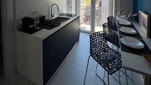 A modern kitchen with a central island, a built-in microwave, and a dining area with a black chair and white plates. - Poerio Station Rooms & Apartment  (Naples)