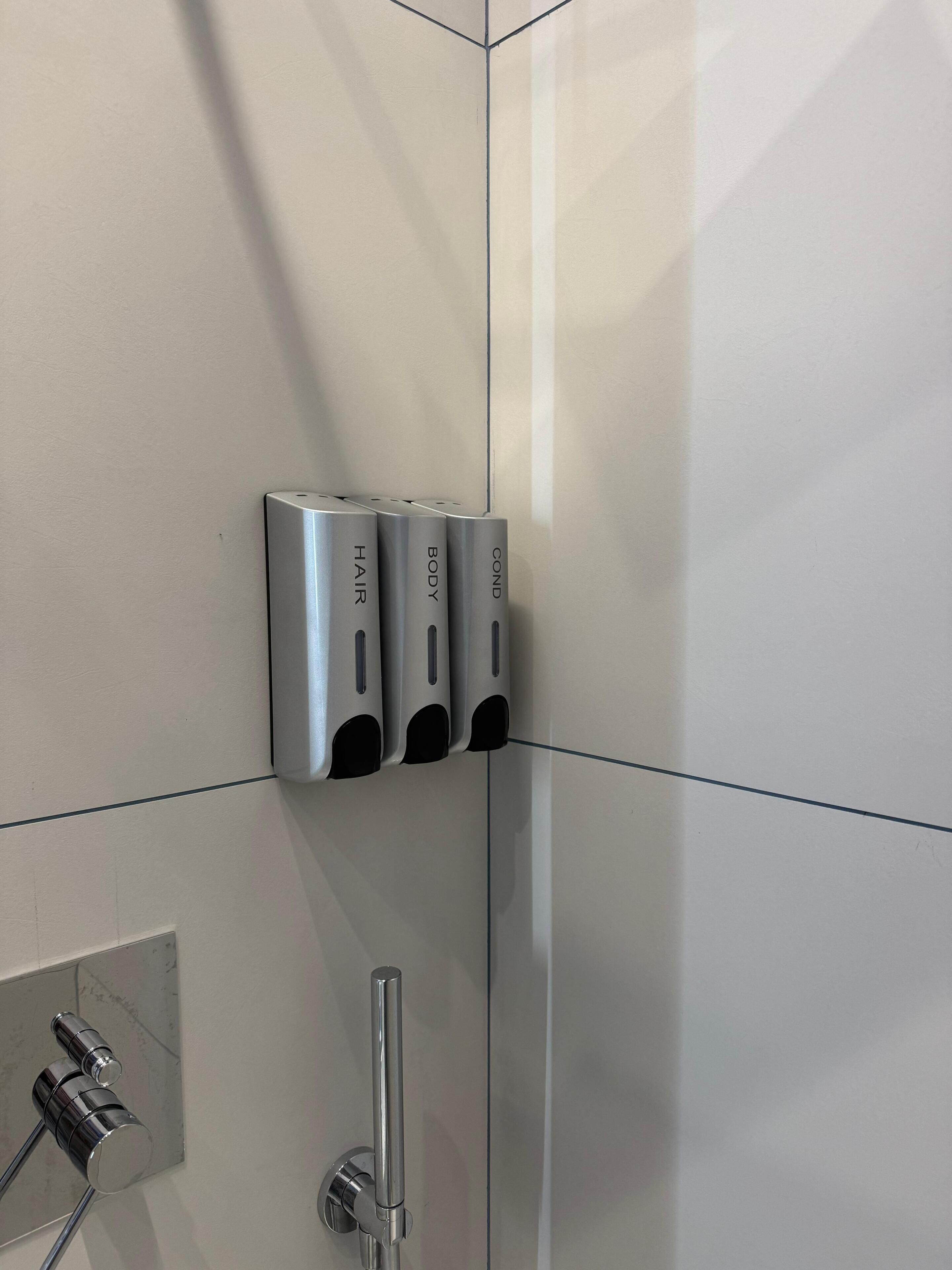 Un baño con un secamanos, un perchero para toallas y un cabezal de ducha.