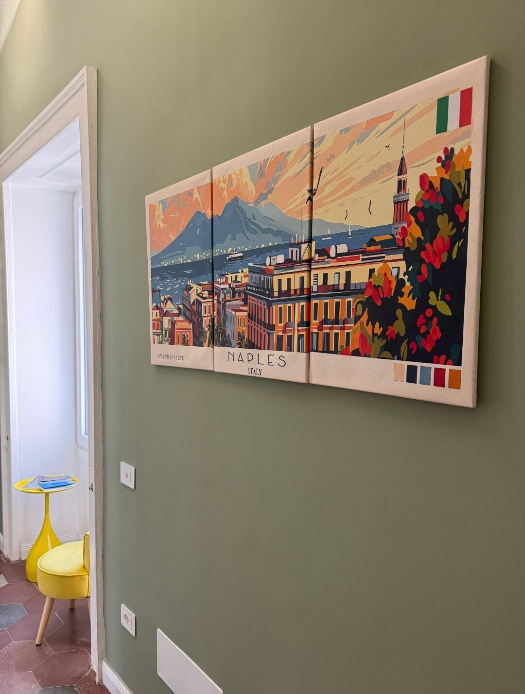A wall with a colorful painting of Naples, Italy, featuring buildings, mountains, and a flag.