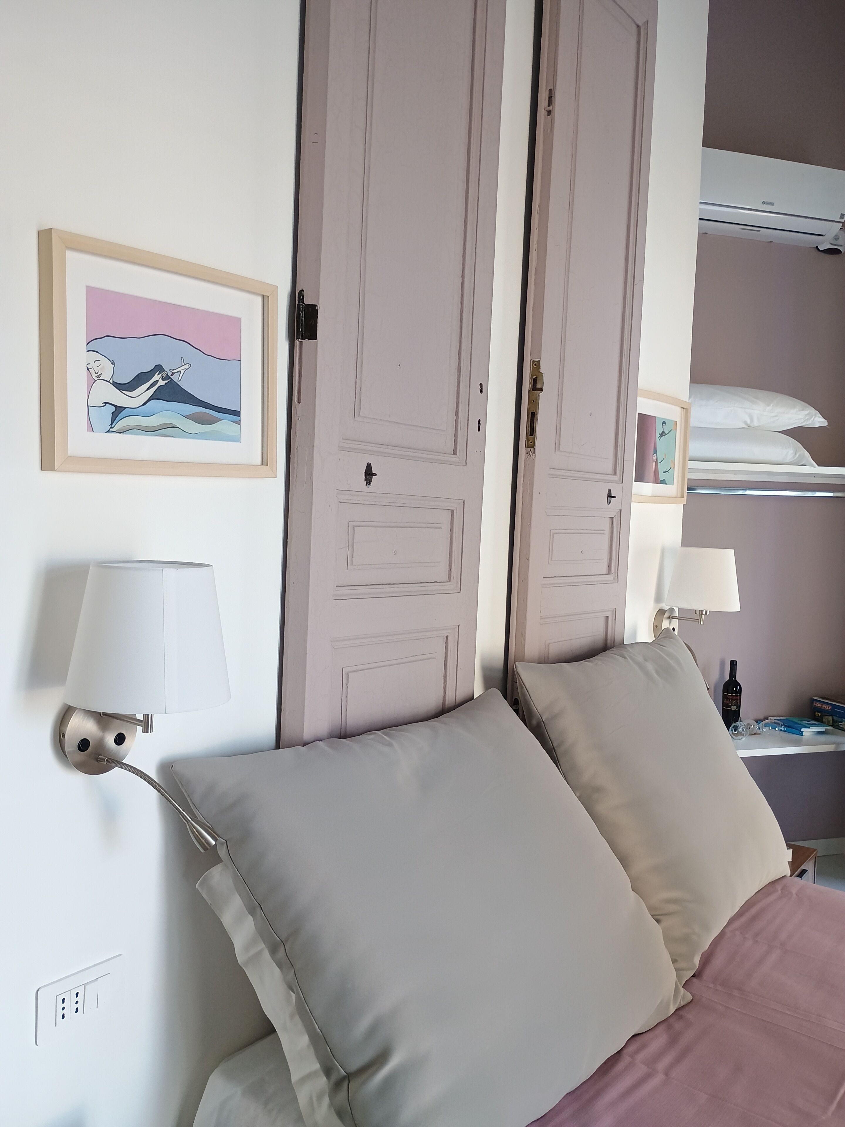 A bedroom with a bed, two bedside lamps, a framed picture, a bunk bed, and a wall-mounted air conditioner.