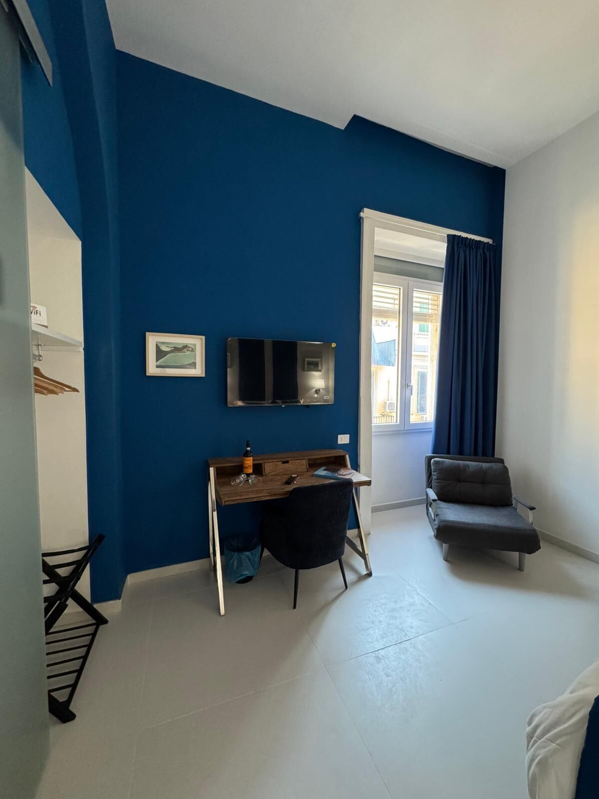Een kamer met een blauwe wand, een houten bureau, een stoel, een televisie en een raam met gordijnen.