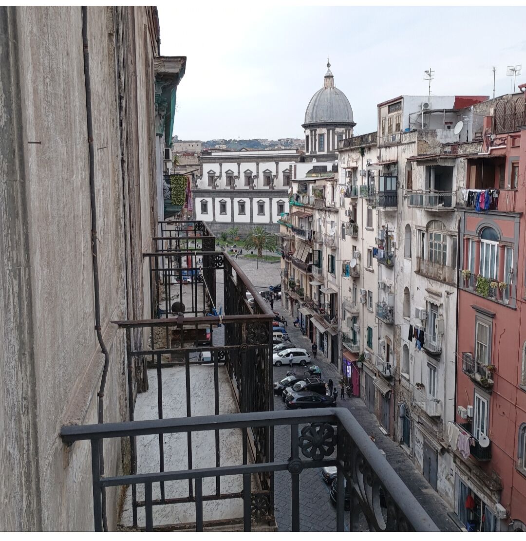 A narrow street with buildings on both sides, a prominent dome structure in the distance, and a metal railing in the foreground.