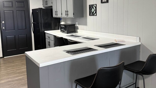 Una cocina moderna con gabinetes grises, una encimera blanca y dos taburetes negros.