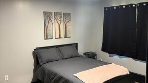 Un dormitorio con cama, mesita de noche, televisor montado en la pared y ventana con cortinas.