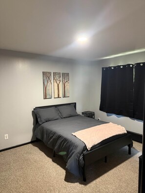A bedroom with a bed, a nightstand, a wall-mounted TV, and a window with curtains.