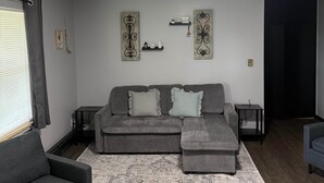 Una sala de estar con un sofá gris, un sillón gris, un tapete estampado y obras de arte en la pared.
