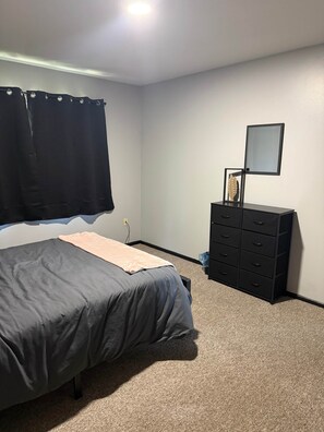 Un dormitorio con cama, cómoda, espejo y ventana con cortinas.