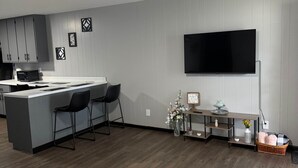 Una cocina moderna con una isla central, taburetes de bar, un televisor de pantalla plana y un comedor con alfombra estampada.