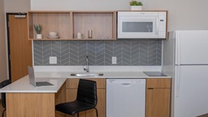 A compact kitchen with a microwave, dishwasher, and a small dining area with a chair.