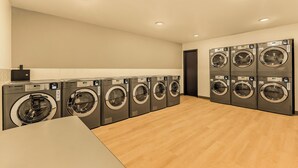 A laundry room with multiple washing machines, wooden flooring, and recessed ceiling lights.