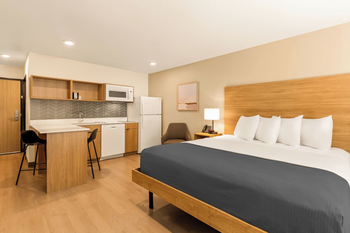 A hotel room with a bed, a desk with a chair, a microwave, a refrigerator, and a small seating area with a chair.