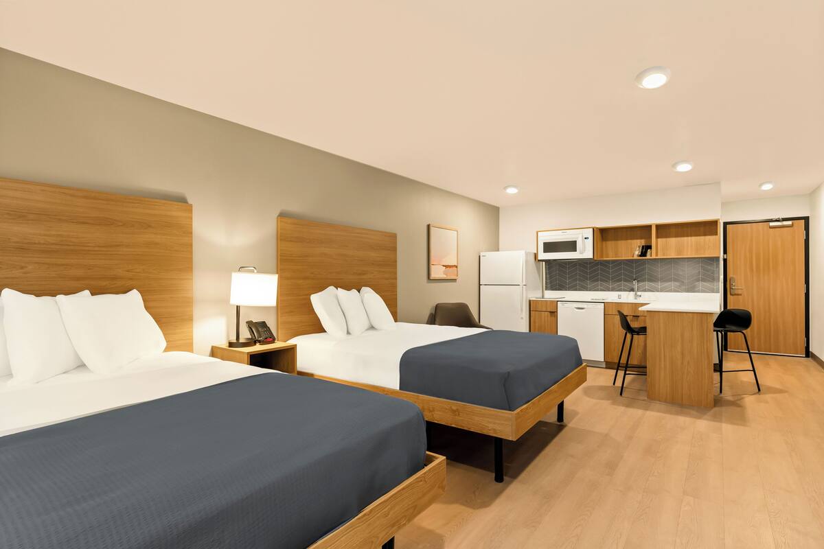A hotel room with two beds, a desk, a microwave, and a small kitchenette.