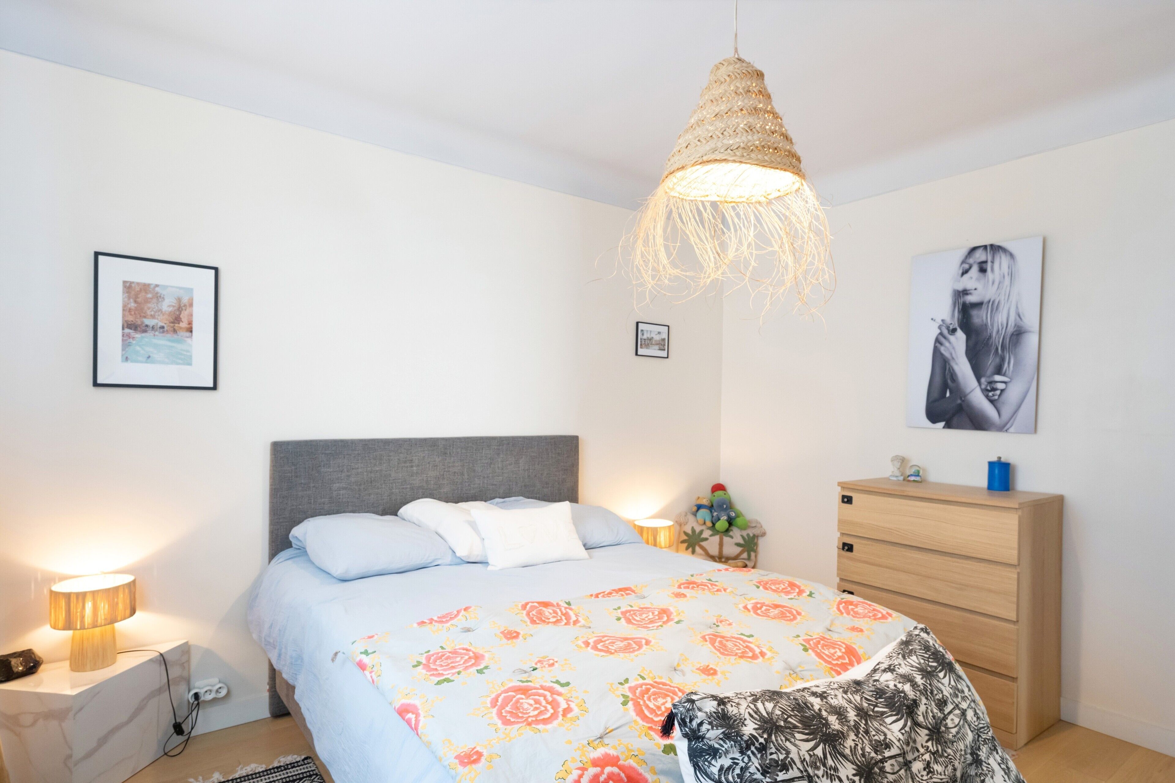 Een slaapkamer met een bed, nachtkastjes, een dressoir en wanddecoratie.