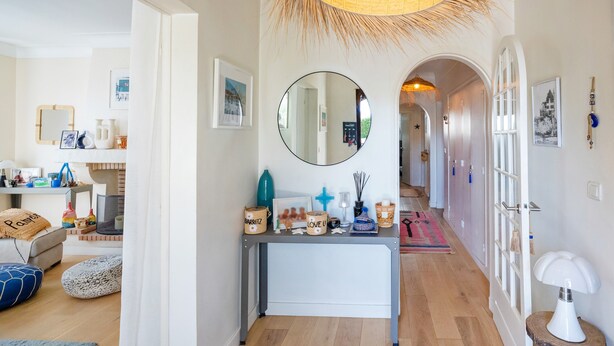 A hallway with a round mirror, a bench, and a table with various items.