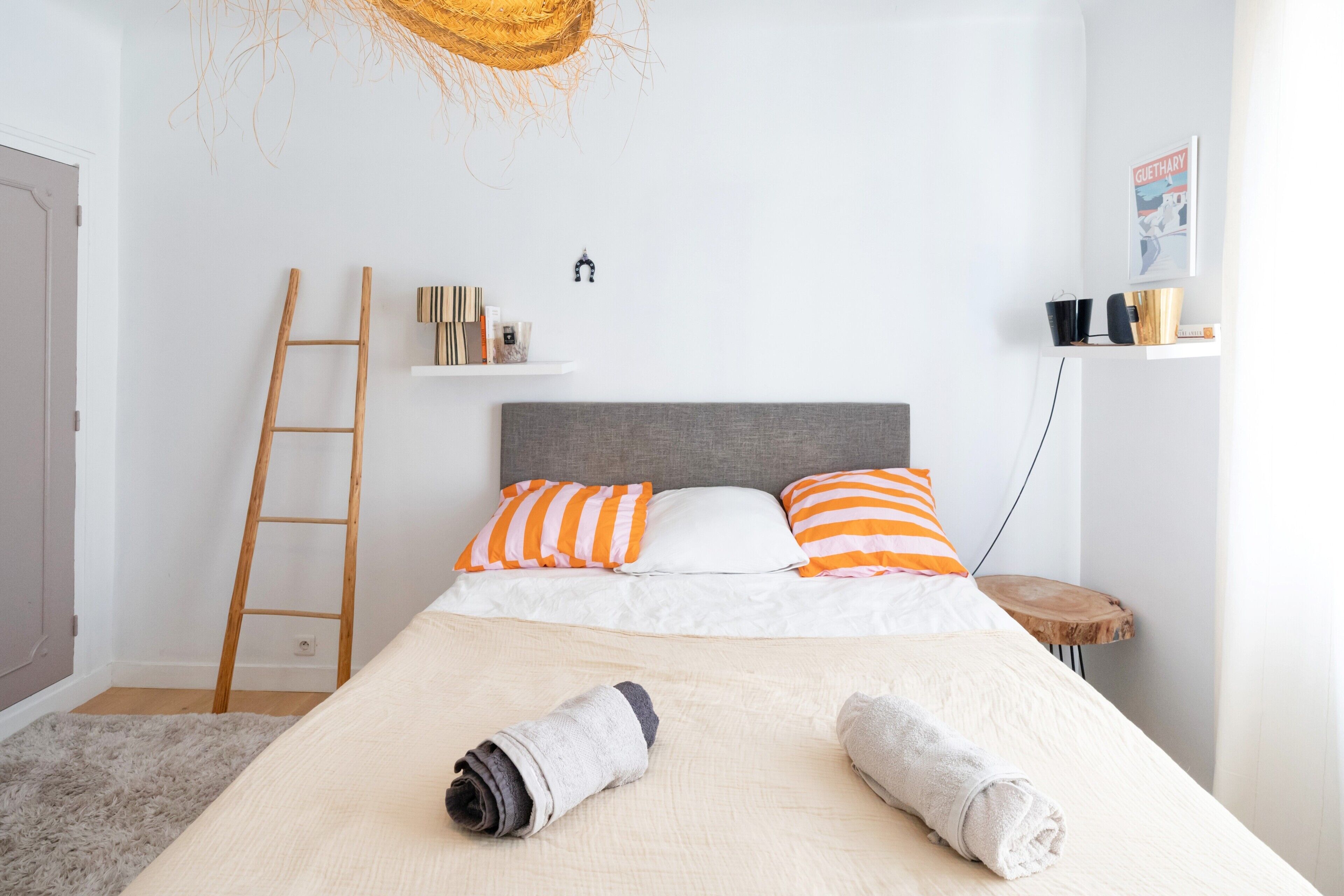 A bedroom with a bed, pillows, a ladder, a shelf with books, and a small table.
