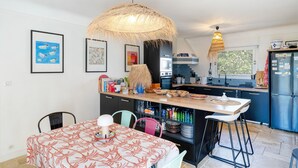 A modern kitchen with a central island, bar stools, and a dining table with a patterned tablecloth.