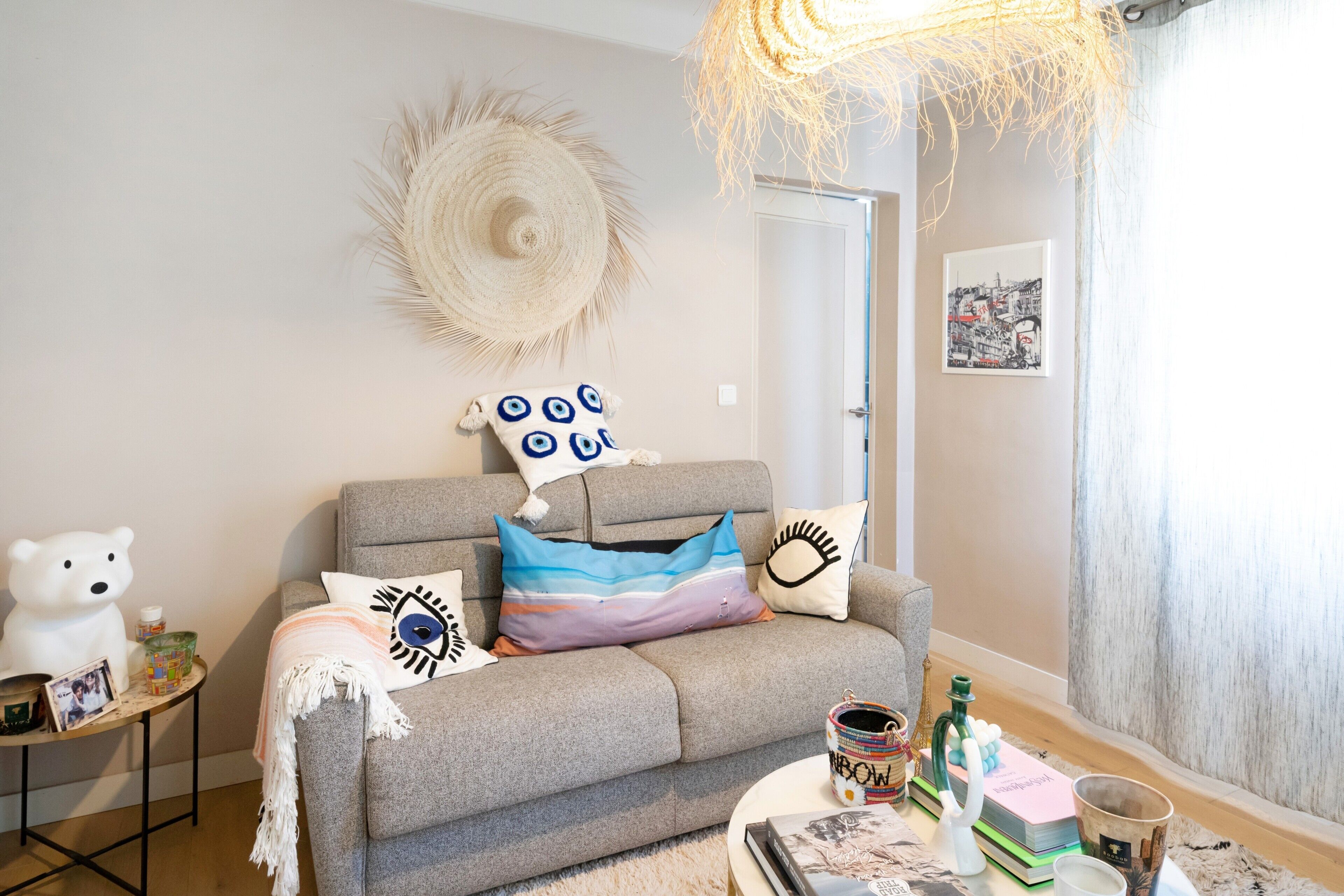 Una sala de estar acogedora con un sofá gris, una escultura de oso blanco, un tapiz de pared tejido y una mesa de centro redonda con libros y objetos decorativos.