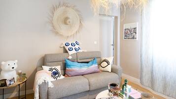 Una sala de estar acogedora con un sofá gris, una escultura de oso blanco, un tapiz de pared tejido y una mesa de centro redonda con libros y objetos decorativos.