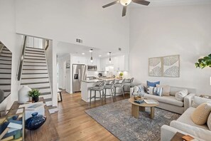 A modern living room with a sofa, coffee table, and a staircase leading to a kitchen area. - Enjoy our beautifully renovated Gulf-view condo in West PCB! (Panama City Beach)