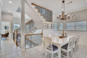 A spacious dining area with a white table and chairs, a staircase with wooden railings, and a chandelier. - Princess of Monaco (Miramar Beach)